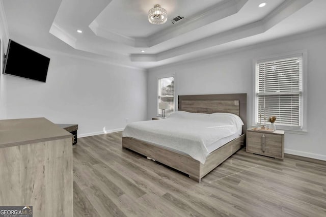 bedroom featuring crown molding, light hardwood / wood-style floors, and a raised ceiling