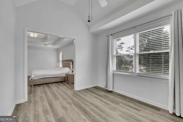 unfurnished bedroom featuring vaulted ceiling, ceiling fan, light wood-type flooring, and a tray ceiling