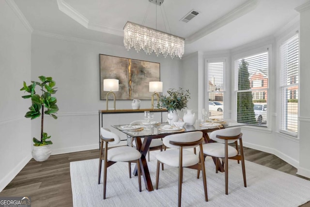 dining space with a raised ceiling, ornamental molding, hardwood / wood-style flooring, and an inviting chandelier