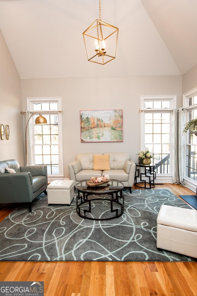 living room with hardwood / wood-style flooring, plenty of natural light, high vaulted ceiling, and a notable chandelier