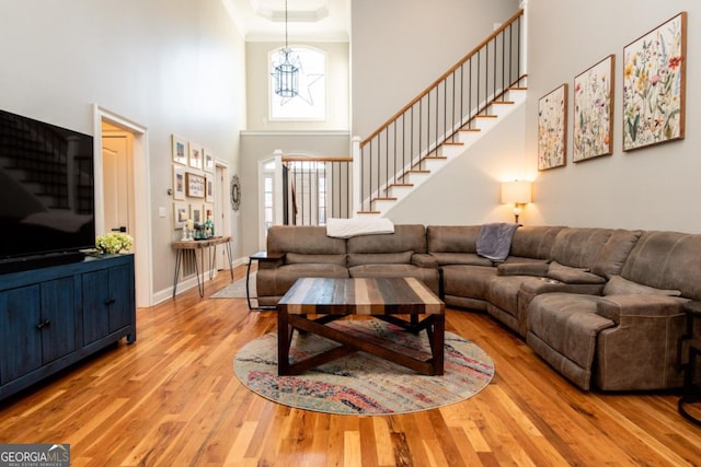 living room featuring a notable chandelier, ornamental molding, a towering ceiling, and light wood-type flooring