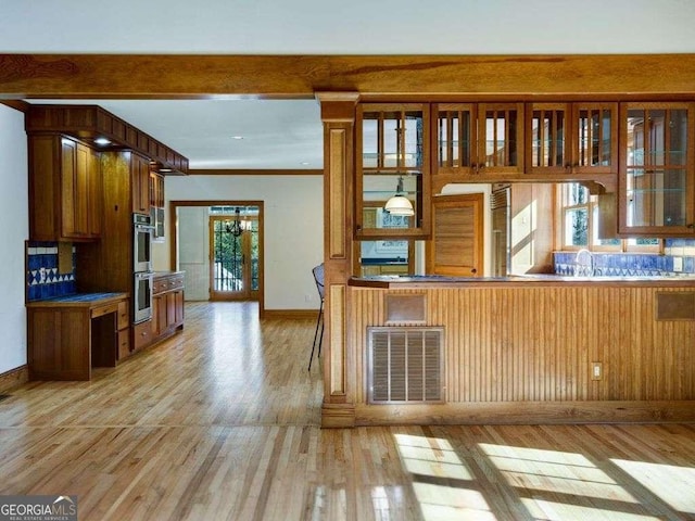 kitchen with crown molding, stainless steel double oven, kitchen peninsula, and light hardwood / wood-style flooring