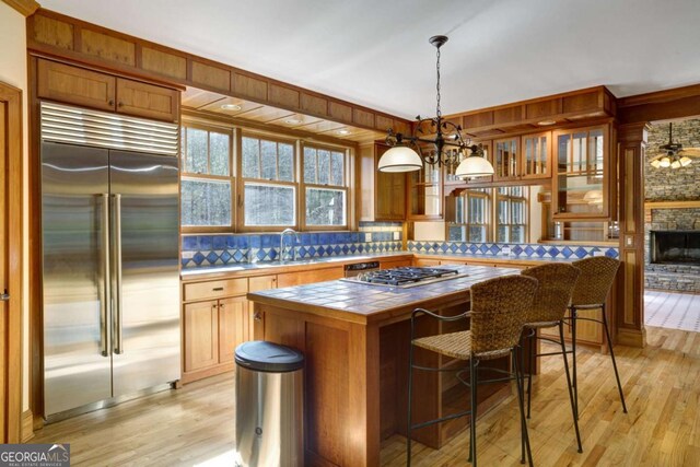 kitchen featuring a kitchen island, decorative light fixtures, tile counters, stainless steel appliances, and light hardwood / wood-style flooring