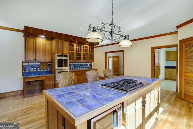 kitchen featuring stainless steel appliances, decorative light fixtures, a kitchen island, and light hardwood / wood-style flooring