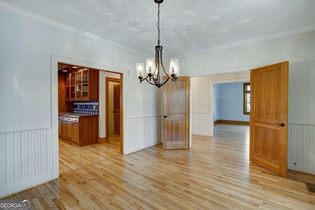 unfurnished dining area with an inviting chandelier, ornamental molding, and light hardwood / wood-style floors