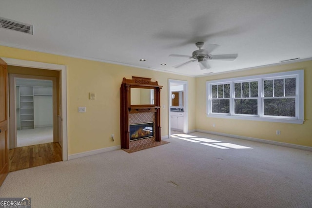 unfurnished living room with a tile fireplace, light carpet, ceiling fan, and crown molding