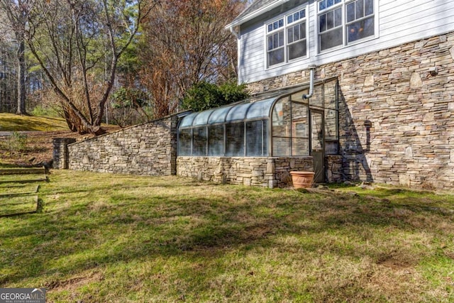 view of side of property with a lawn, a sunroom, and stone siding