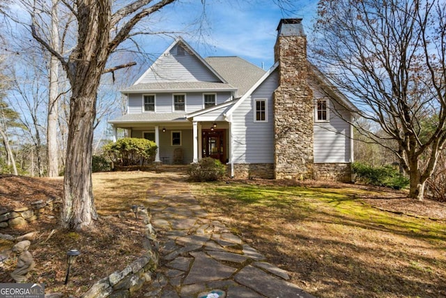 traditional-style house featuring a shingled roof, stone siding, covered porch, and a chimney