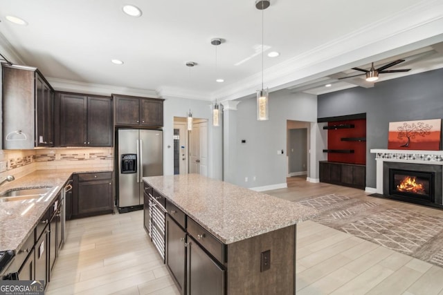 kitchen featuring pendant lighting, dark brown cabinets, a center island, stainless steel refrigerator with ice dispenser, and light stone countertops