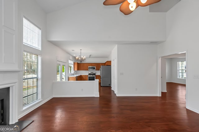 unfurnished living room featuring a towering ceiling, sink, dark hardwood / wood-style flooring, and ceiling fan with notable chandelier