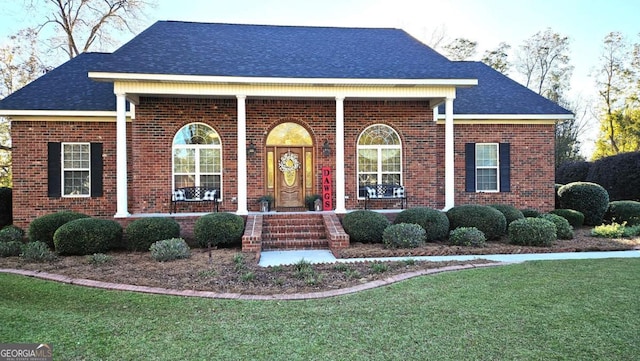 view of front facade featuring covered porch, roof with shingles, a front lawn, and brick siding