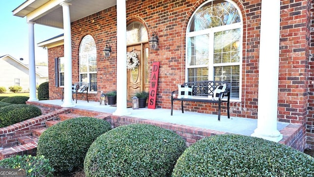 view of exterior entry featuring a porch and brick siding