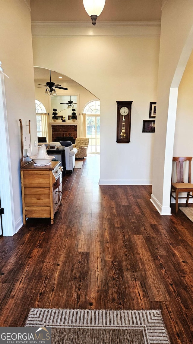 corridor with arched walkways, dark wood-type flooring, plenty of natural light, and crown molding