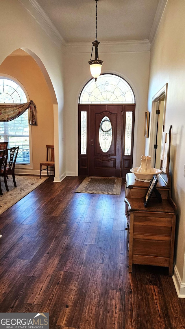 foyer entrance with baseboards, crown molding, arched walkways, and dark wood-style flooring