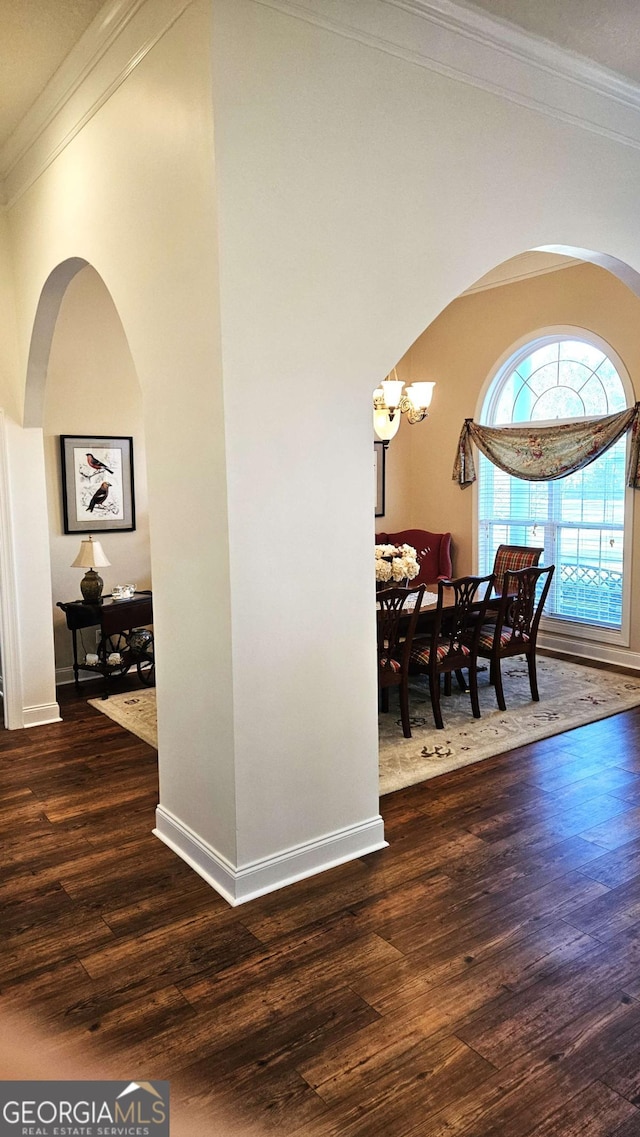 interior space with baseboards, arched walkways, ornamental molding, dark wood-type flooring, and a chandelier