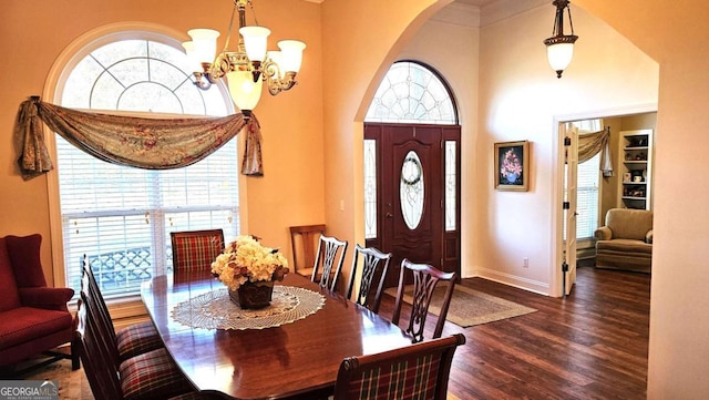 dining space featuring arched walkways, a notable chandelier, wood finished floors, a towering ceiling, and baseboards