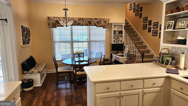 kitchen with dark wood finished floors, light countertops, hanging light fixtures, ornamental molding, and a peninsula