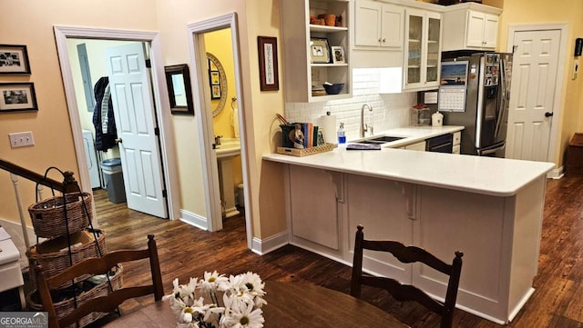 kitchen with glass insert cabinets, a breakfast bar, light countertops, stainless steel refrigerator with ice dispenser, and a sink