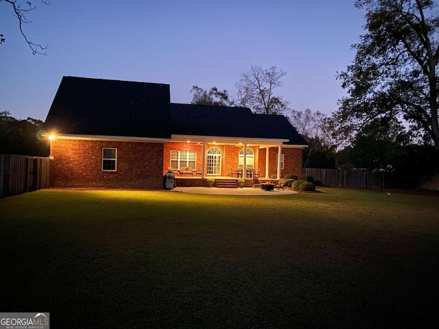 back of property at dusk with brick siding, a lawn, and fence