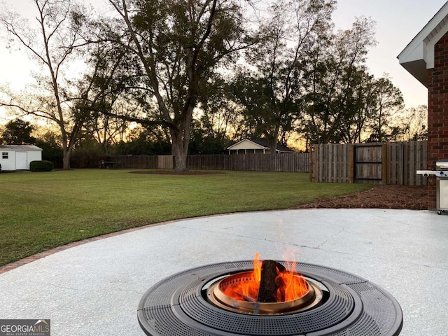 view of patio with a storage shed, an outdoor fire pit, area for grilling, fence, and an outdoor structure