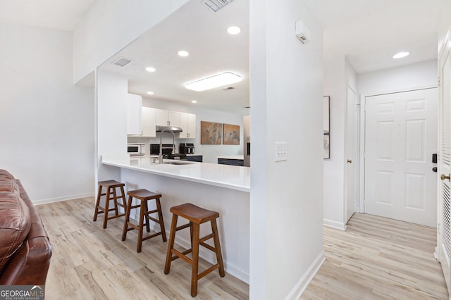 kitchen with a kitchen bar, sink, white cabinetry, light wood-type flooring, and kitchen peninsula