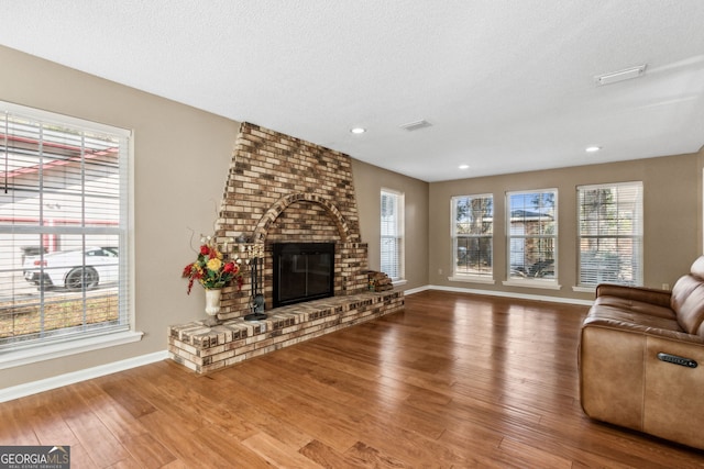 living room featuring wood-type flooring, a brick fireplace, and a textured ceiling