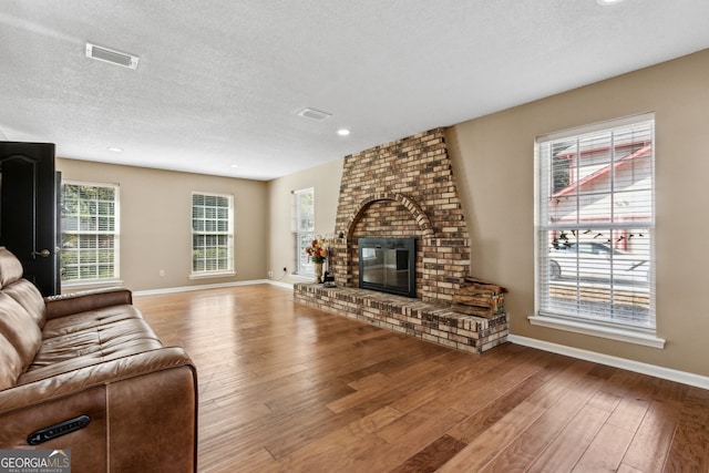 living room with hardwood / wood-style floors, a textured ceiling, and a brick fireplace