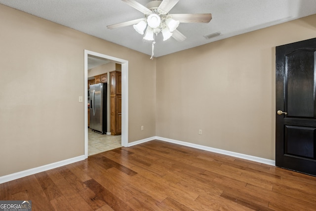 unfurnished room with ceiling fan, a textured ceiling, and light wood-type flooring