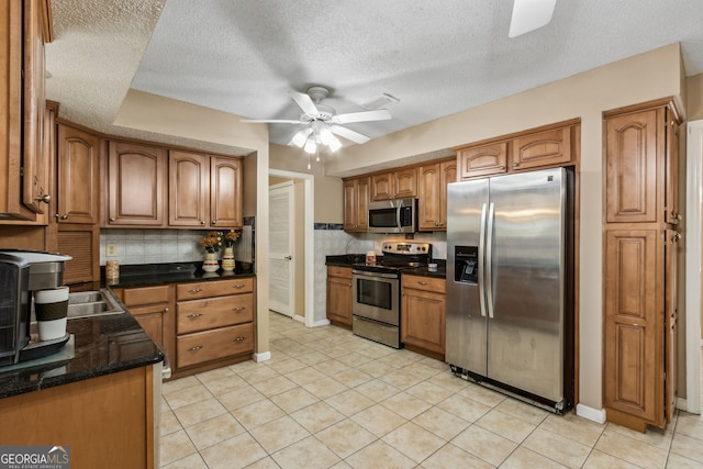 kitchen featuring light tile patterned floors, ceiling fan, appliances with stainless steel finishes, dark stone countertops, and decorative backsplash