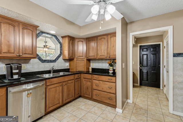 kitchen with sink, dishwasher, a textured ceiling, light tile patterned flooring, and dark stone counters