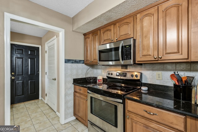 kitchen with appliances with stainless steel finishes, light tile patterned floors, a textured ceiling, and dark stone counters