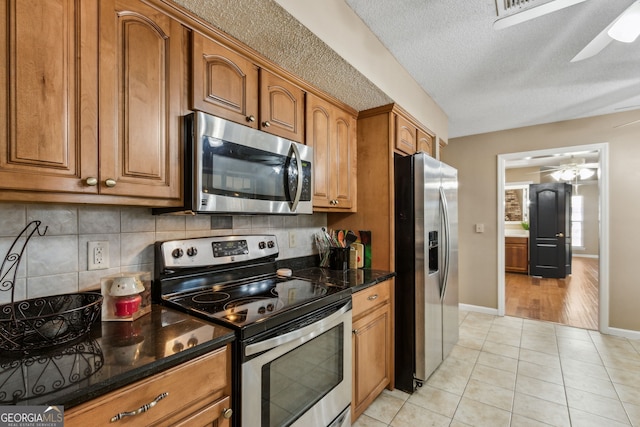 kitchen featuring backsplash, stainless steel appliances, light tile patterned flooring, and dark stone counters