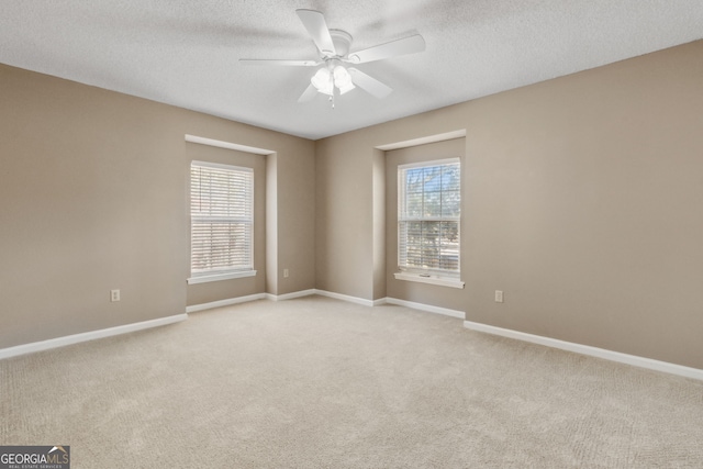 spare room with a healthy amount of sunlight, light colored carpet, a textured ceiling, and ceiling fan