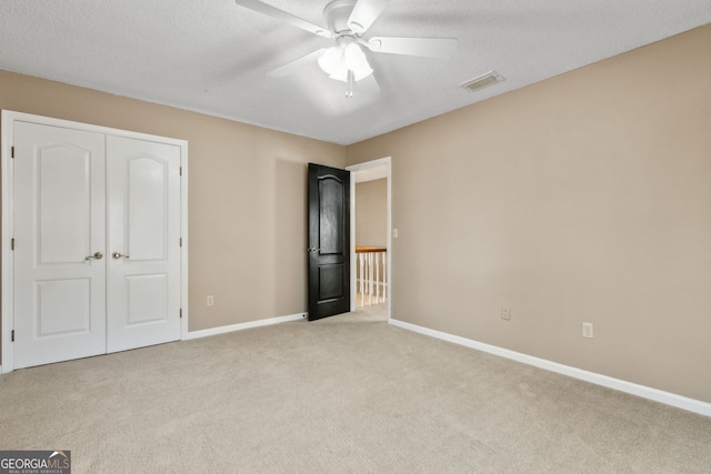 unfurnished bedroom with ceiling fan, a closet, light carpet, and a textured ceiling