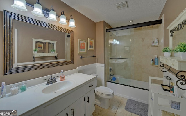 full bathroom with shower / bath combination with glass door, tile patterned flooring, vanity, a textured ceiling, and toilet