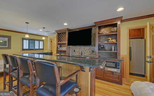 kitchen with stainless steel refrigerator, black microwave, a kitchen bar, hanging light fixtures, and kitchen peninsula