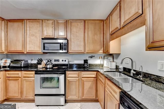 kitchen with stainless steel appliances, sink, dark stone countertops, and light tile patterned floors