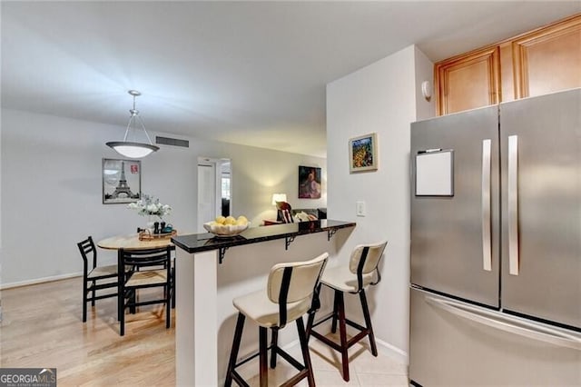 kitchen featuring a breakfast bar area, light wood-type flooring, stainless steel refrigerator, kitchen peninsula, and pendant lighting