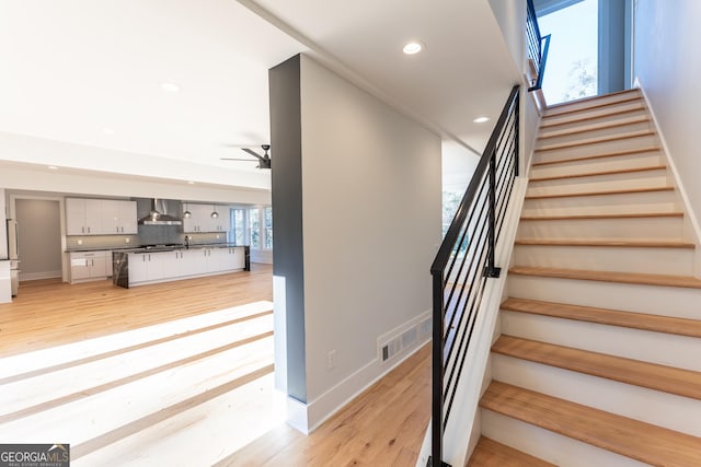 staircase with wood-type flooring, sink, and ceiling fan