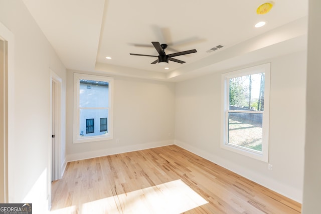 unfurnished room featuring a raised ceiling, ceiling fan, and light hardwood / wood-style floors