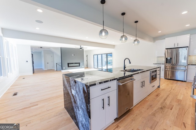 kitchen with sink, hanging light fixtures, stainless steel appliances, a kitchen island with sink, and white cabinets