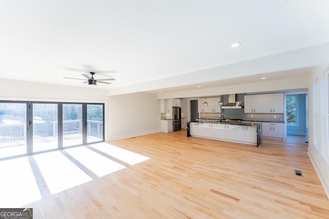 kitchen featuring a kitchen island, white cabinets, backsplash, wall chimney range hood, and light wood-type flooring