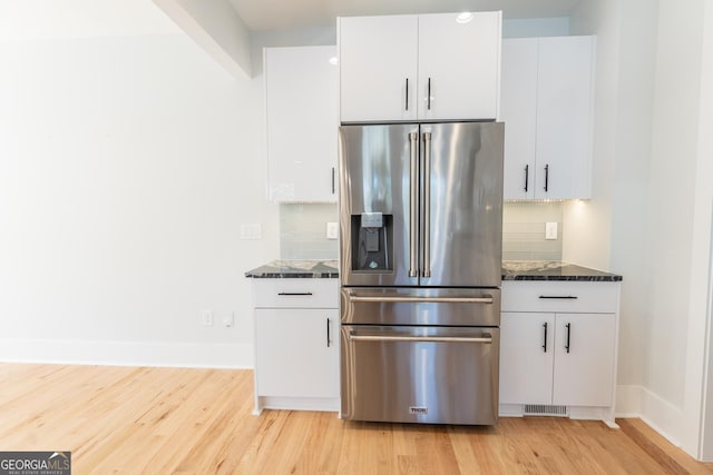 kitchen featuring white cabinetry, tasteful backsplash, light hardwood / wood-style floors, high quality fridge, and dark stone counters