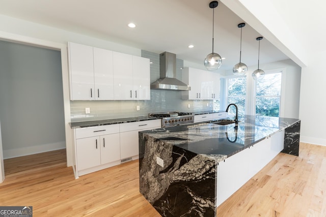 kitchen with pendant lighting, wall chimney range hood, white cabinets, and a spacious island