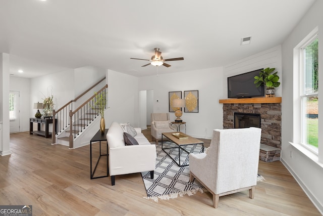 living area featuring stairs, a stone fireplace, baseboards, and light wood-type flooring