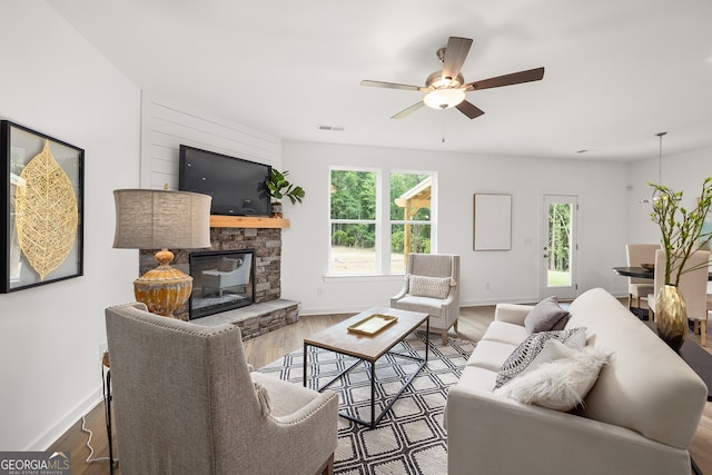 living room featuring visible vents, ceiling fan, baseboards, a stone fireplace, and wood finished floors