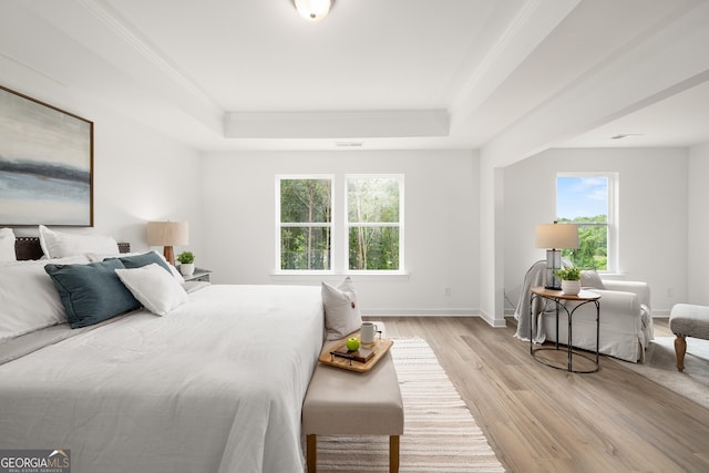 bedroom with visible vents, a raised ceiling, ornamental molding, light wood-style floors, and baseboards