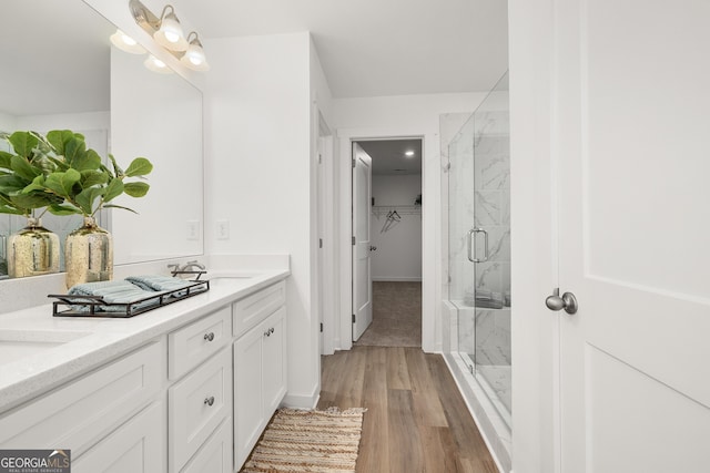 bathroom with double vanity, wood finished floors, a marble finish shower, and a sink