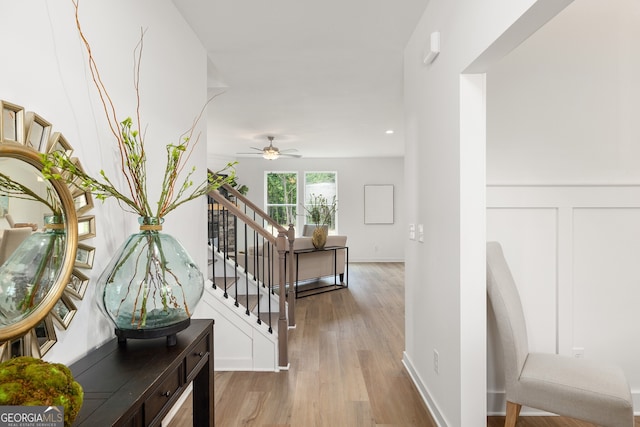 hallway featuring a wainscoted wall, wood finished floors, stairs, and a decorative wall