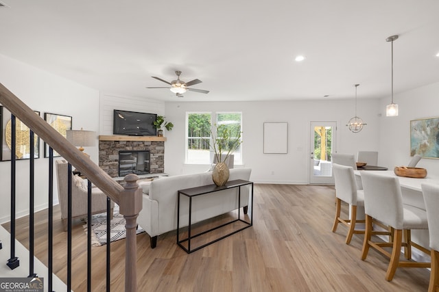 living room featuring a wealth of natural light, light wood-style floors, stairs, and ceiling fan with notable chandelier